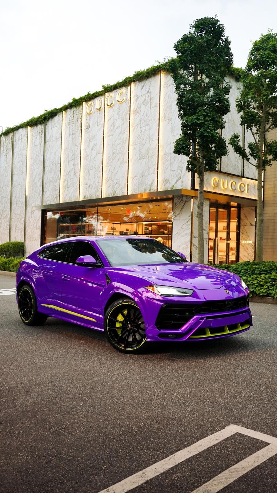 Purple Lamborghini Urus with lime green trim parked outside a designer boutique